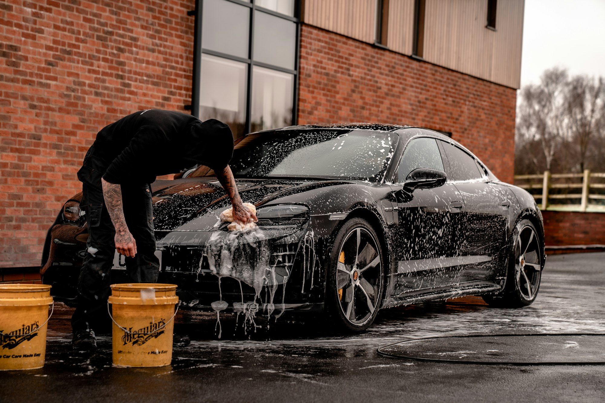 A car covered in foam being washed by hand
