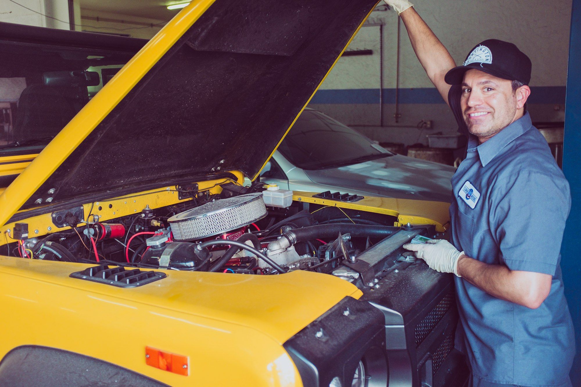 A smiling mechanic leaning over the open bonnet of a car